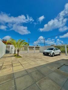 a white car parked in a parking lot with a palm tree at Bangalô com tudo privativo em Tamandaré/PE in Tamandaré