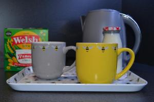 two coffee mugs on a plate next to a container of milk at Greenfield Studio in Cardiff