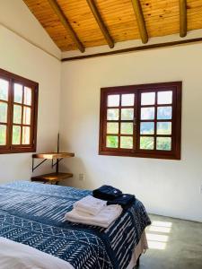 um quarto com uma cama e duas janelas em Chale Vale das Cachoeiras em Capitólio