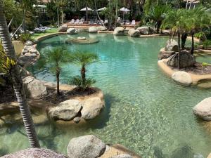 einen Pool in einem Resort mit Palmen und Felsen in der Unterkunft Reef Resort Villas Port Douglas in Port Douglas