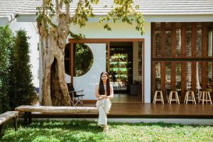 una mujer sentada en un banco frente a una casa en Nainan resotel ในน่าน รีโซเทล, en Nan