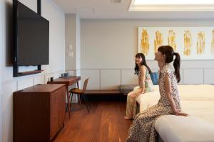 dos mujeres sentadas en camas en una habitación de hospital en Lequ Okinawa Chatan Spa ＆ Resort, en Chatan