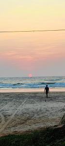 um homem andando na praia ao pôr do sol em Blue Pearl Beach Guest House em Māvalli