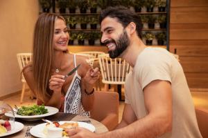 Ein Mann und eine Frau sitzen am Tisch und essen Essen. in der Unterkunft Fujairah Rotana Resort & Spa - Al Aqah Beach in Al Aqah
