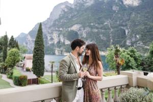 a man and woman standing on a balcony with a wine glass at Lido Palace - The Leading Hotels of the World in Riva del Garda