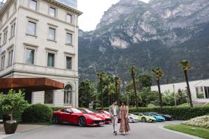 a couple walking in front of a building with cars at Lido Palace - The Leading Hotels of the World in Riva del Garda