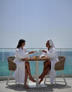 two women in white sitting at a table with food at 360ᵒ Luxury View Collection - Adults Only in Limenaria