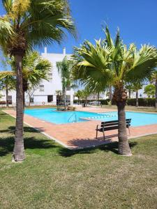 a swimming pool with a bench between two palm trees at Luxury Ground Floor Apartment at Golf Resort Condado de Alhama with Private Garden & Pools in El Romero