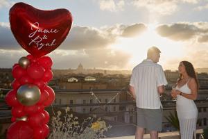 un hombre y una mujer de pie en un balcón con un globo cardíaco en VIVILO ROMA TREVI - LUXURY EXPERIENCE - PRIVATE JACUZZI on TERRACE - INSANE VIEW en Roma