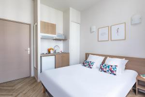 a white bedroom with a bed and a small kitchen at Appart’City Confort Reims Centre in Reims