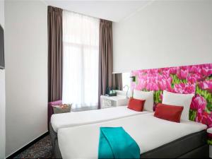 una camera d'albergo con un grande letto con fiori rosa di ibis Styles Amsterdam City ad Amsterdam