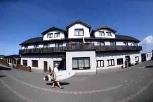 a man carrying a surfboard in front of a building at Pokoje i Domki DRAGA in Jastarnia