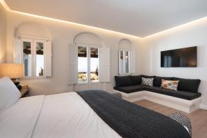 ein Schlafzimmer mit einem Bett, einem Sofa und Fenstern in der Unterkunft NĒRO Suites by NOMÉE Hospitality Group in Imerovigli
