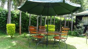 a table and chairs under a green umbrella at Wooden Knee Cottages Nanyuki in Nanyuki