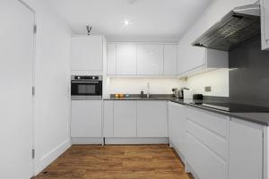 a white kitchen with white cabinets and black appliances at Manor House Studios By Morethanstays in London