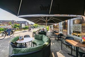 un patio al aire libre con mesas, sillas y una sombrilla en Hotel Over de Brug, en Haastrecht