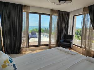 een slaapkamer met een bed en een stoel en grote ramen bij Marina Sarafovo in Boergas