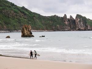 three people walking on the beach with their surfboards at wecamp Cudillero in El Pito