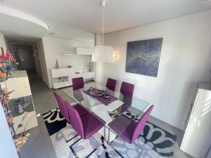 une salle à manger avec une table en verre et des chaises violettes dans l'établissement Stylish apartment in Guardamar, à Guardamar del Segura