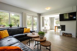 a living room with a black leather couch and a fireplace at Luxe Villa Texel 8-10 personen met Sauna Krim 95 in De Cocksdorp