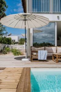 um pátio com um sofá e um guarda-sol ao lado de uma piscina em Villa Possanco, Comporta beach villa em Comporta