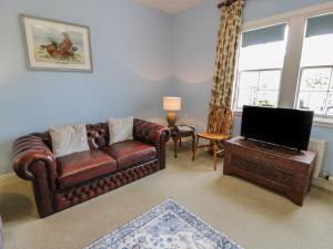 een woonkamer met een leren bank en een televisie bij Fordie East Cottage in Crieff