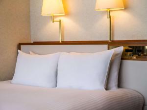 ein Bett mit weißen Kissen und zwei Lichtern darüber in der Unterkunft Grand Mercure Lake Hamana Resort & Spa in Hamamatsu