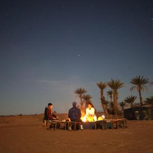 een groep mensen die rond een vuur in de woestijn zitten bij Camp M'hamid Ras N'khal in Mhamid