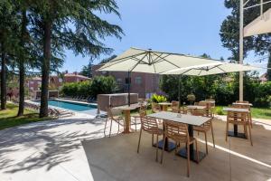 eine Terrasse mit Tischen, Stühlen und einem Sonnenschirm in der Unterkunft Hotel Emaus in Novigrad Istria