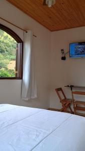 1 dormitorio con cama, ventana y silla en Pousada Casa da montanha en Casimiro de Abreu