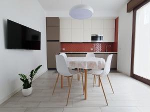 a kitchen with a table with white chairs and a tv at HERON Apartment in Scardovari