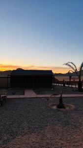 a building in the desert with a sunset in the background at wadi rum fox road camp & jeep tour in Wadi Rum