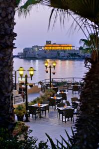 a restaurant with tables and chairs next to a body of water at Marina Hotel Corinthia Beach Resort Malta in St. Julianʼs