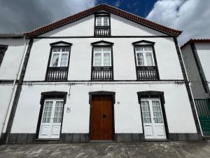 a white house with white windows and a wooden door at O Prior - Aposentos in Urzelina