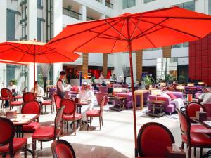 um restaurante com guarda-sóis vermelhos e pessoas sentadas às mesas em Novotel Dammam Business Park em Dammam
