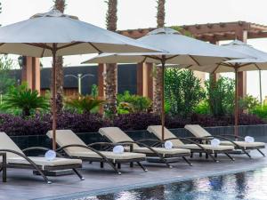 Movenpick Hotel and Residences Riyadh في الرياض: صف من كراسي الصالة والمظلات بجانب المسبح