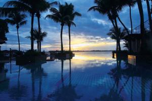 uma piscina com palmeiras e o oceano ao pôr do sol em Taj Malabar Resort & Spa, Cochin. em Cochin