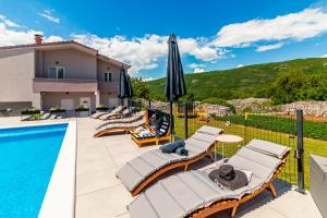 a pool with lounge chairs and umbrellas next to a house at Jackal Holiday House with a heated pool and a jacuzzi in Lovreć
