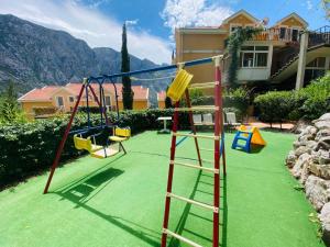 a playground with several swings on a green lawn at Boka Kotorska Apartmani in Gornji Orahovac