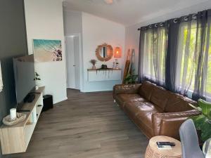 sala de estar con sofá de cuero marrón y ventanas en Tropical Getaway, en Kororo Basin