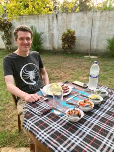 un hombre sentado en una mesa de picnic con comida en Lucky's Homestay en Maho