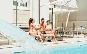 Hotel Regina Elena 57 & Oro Bianco SPA في ريميني: مجموعة اشخاص جالسين على طرف المسبح