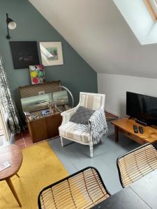 Una sala de estar con una silla y un televisor. en Ô Grenier de l'artiste, en Bazenville