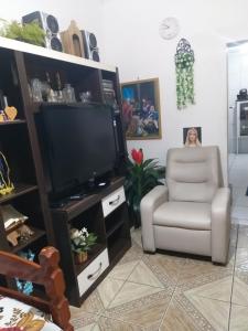 a woman sitting in a chair in a living room with a television at casa vó doca, preço único pela casa inteira,cabem até 10 pessoas ao lado da basilica aparecida in Aparecida