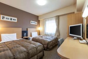Habitación de hotel con 2 camas y escritorio con TV. en Comfort Hotel Obihiro, en Obihiro