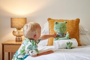 Ein Baby spielt mit einem gefüllten Frosch auf dem Bett in der Unterkunft Residence Vocelova in Prag