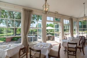 uma sala de jantar com mesas e cadeiras brancas e janelas em Bartley Lodge Hotel em Lyndhurst