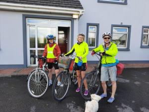 três pessoas de pé com as suas bicicletas e um cão em Kemar House em Belmullet