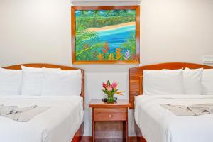 dos camas con sábanas blancas y un jarrón de flores en una mesita de noche en SunBreeze Hotel, en San Pedro