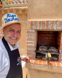 a man wearing a hat and apron standing next to a brick oven at Riad Zouhour in Marrakech